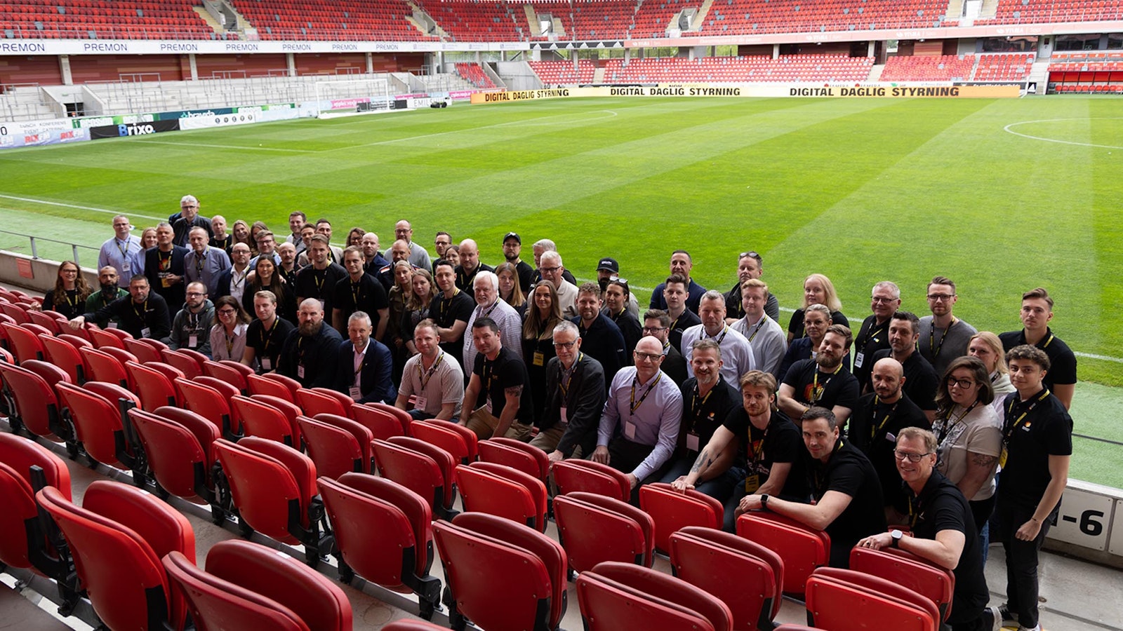 Large group of participants gathered in stadium seats by a football pitch during a Boards on Fire user event.