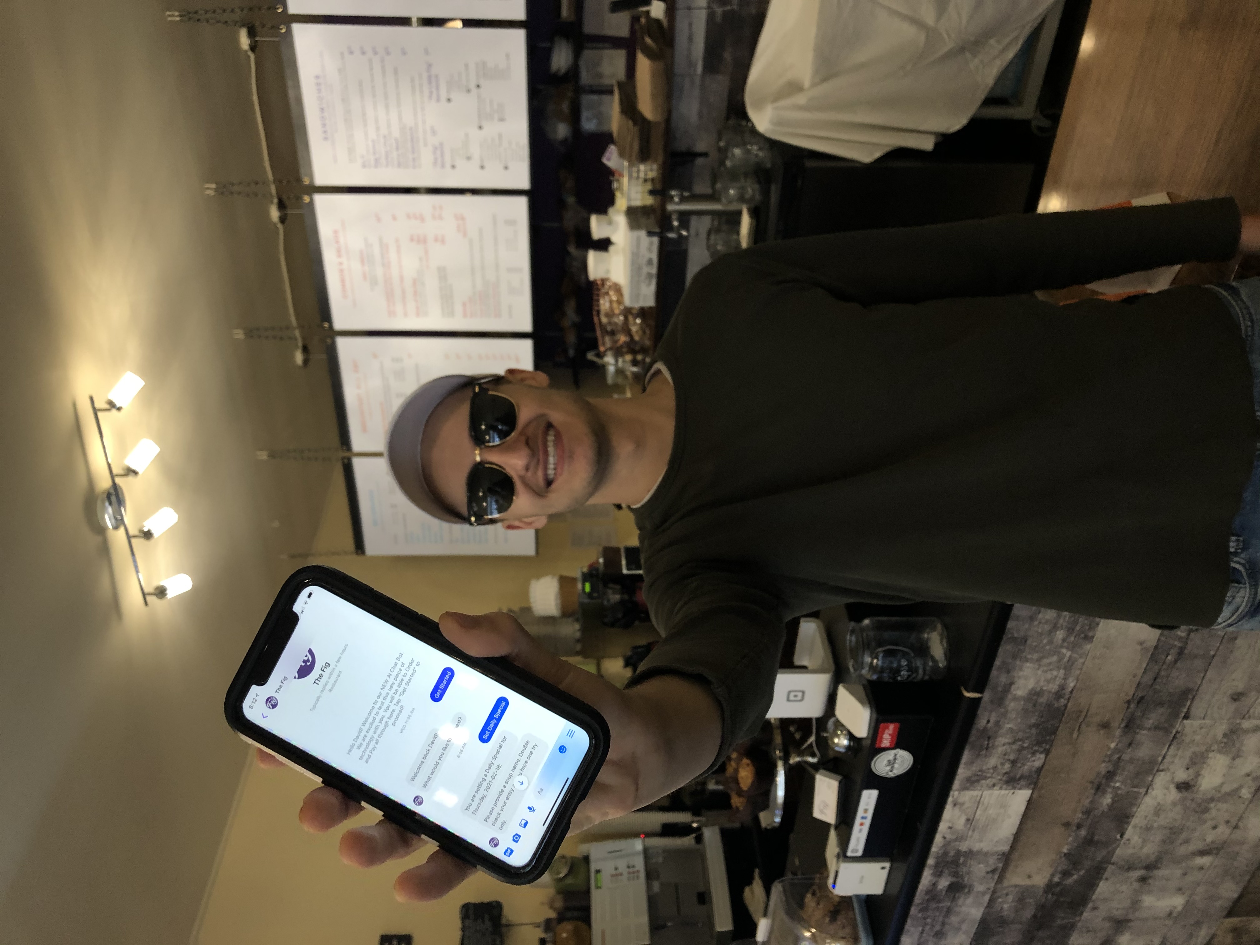 David Scarlatescu the owner of The Fig is holding an iPhone displaying the chatbot in Facebook Messenger
