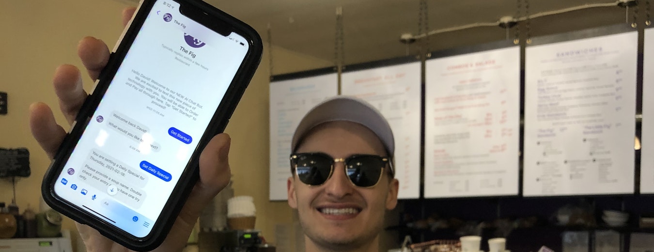 David Scarlatescu the owner of The Fig is holding an iPhone displaying the chatbot in Facebook Messenger