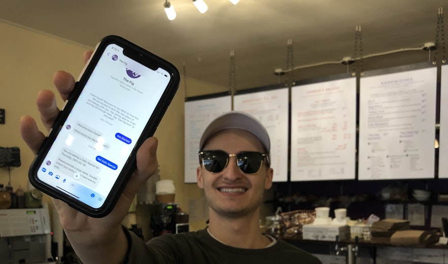 David Scarlatescu the owner of The Fig is holding an iPhone displaying the chatbot in Facebook Messenger