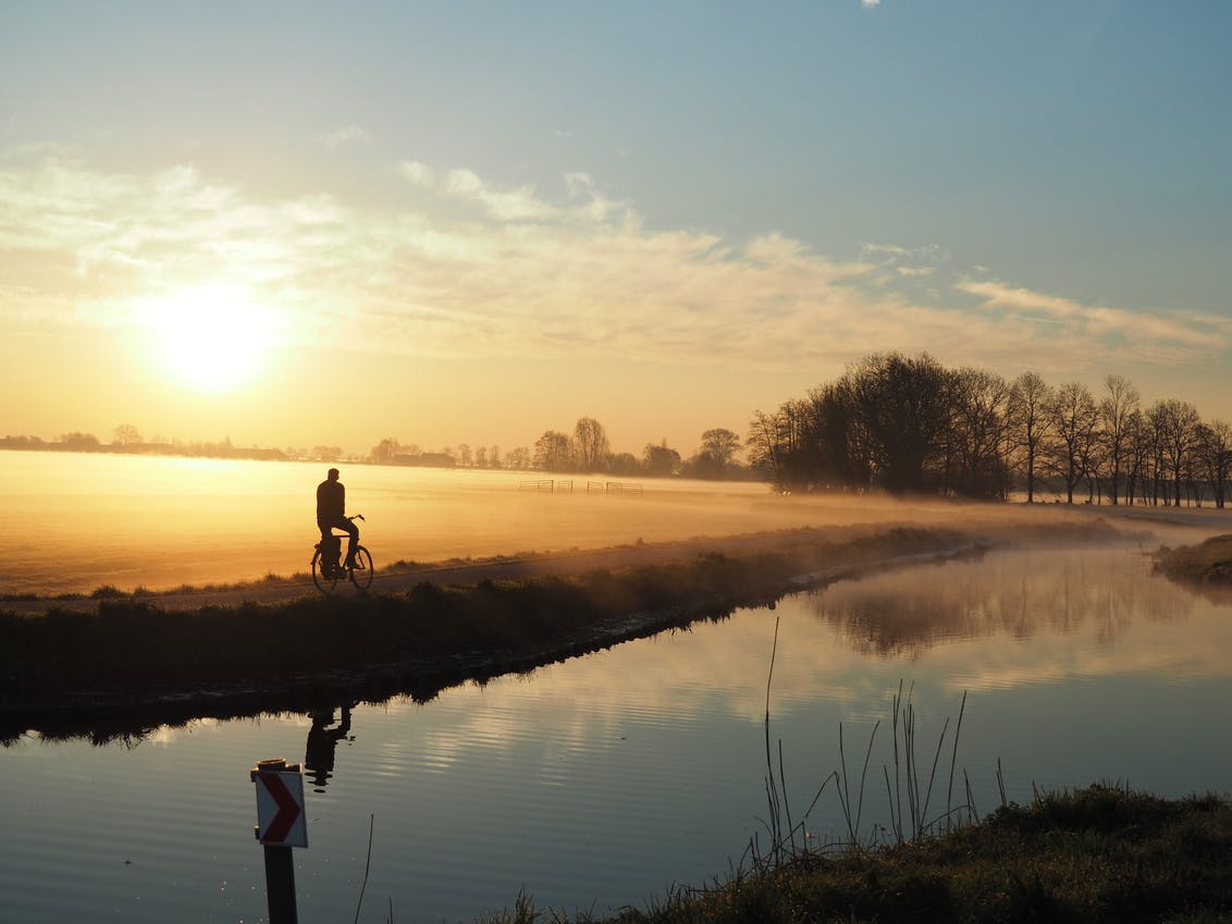 Man fietsend over dijkje tijdens zonsopgang