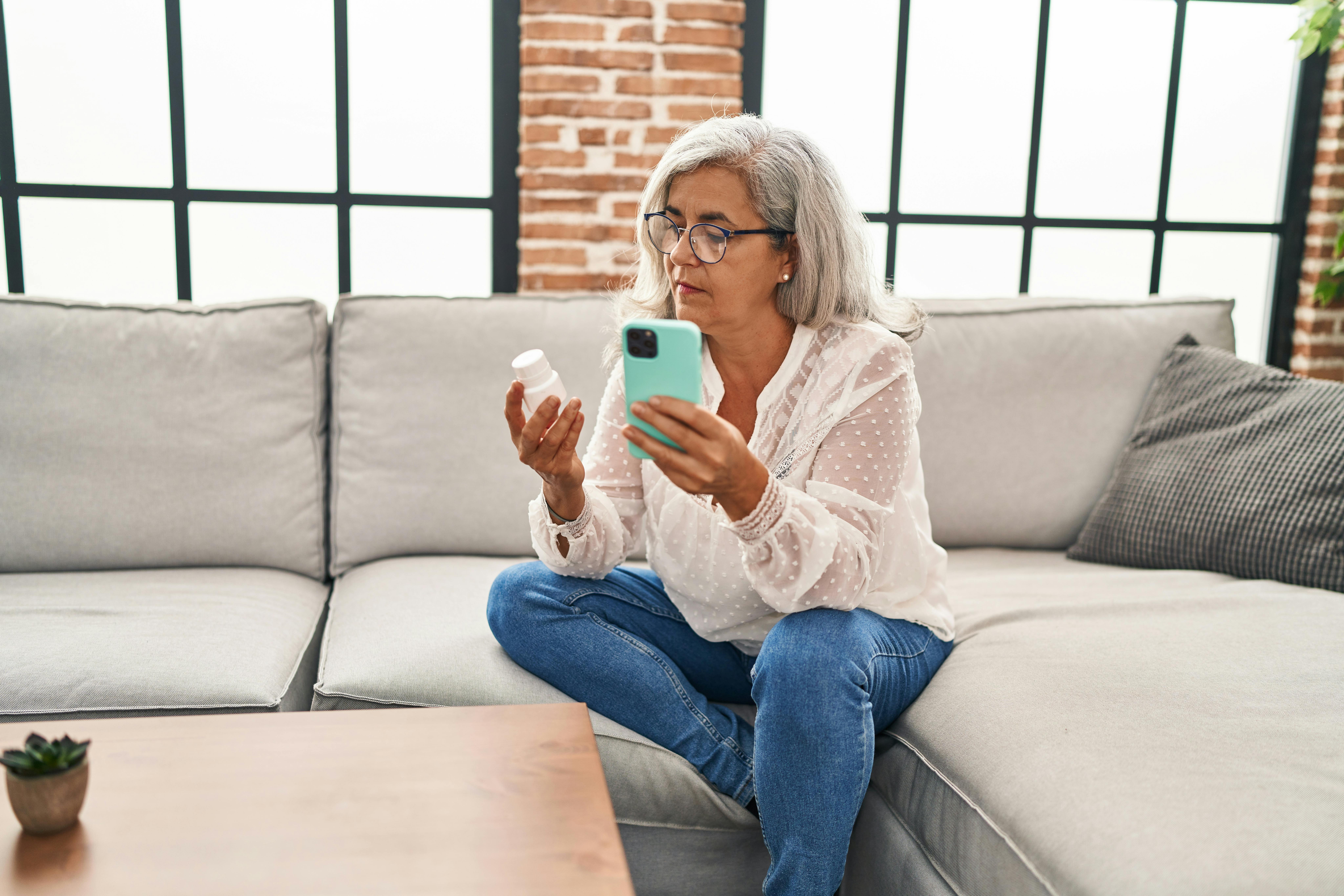 Vrouw met potje medicijnen in de ene hand en een smartphone in de andere hand