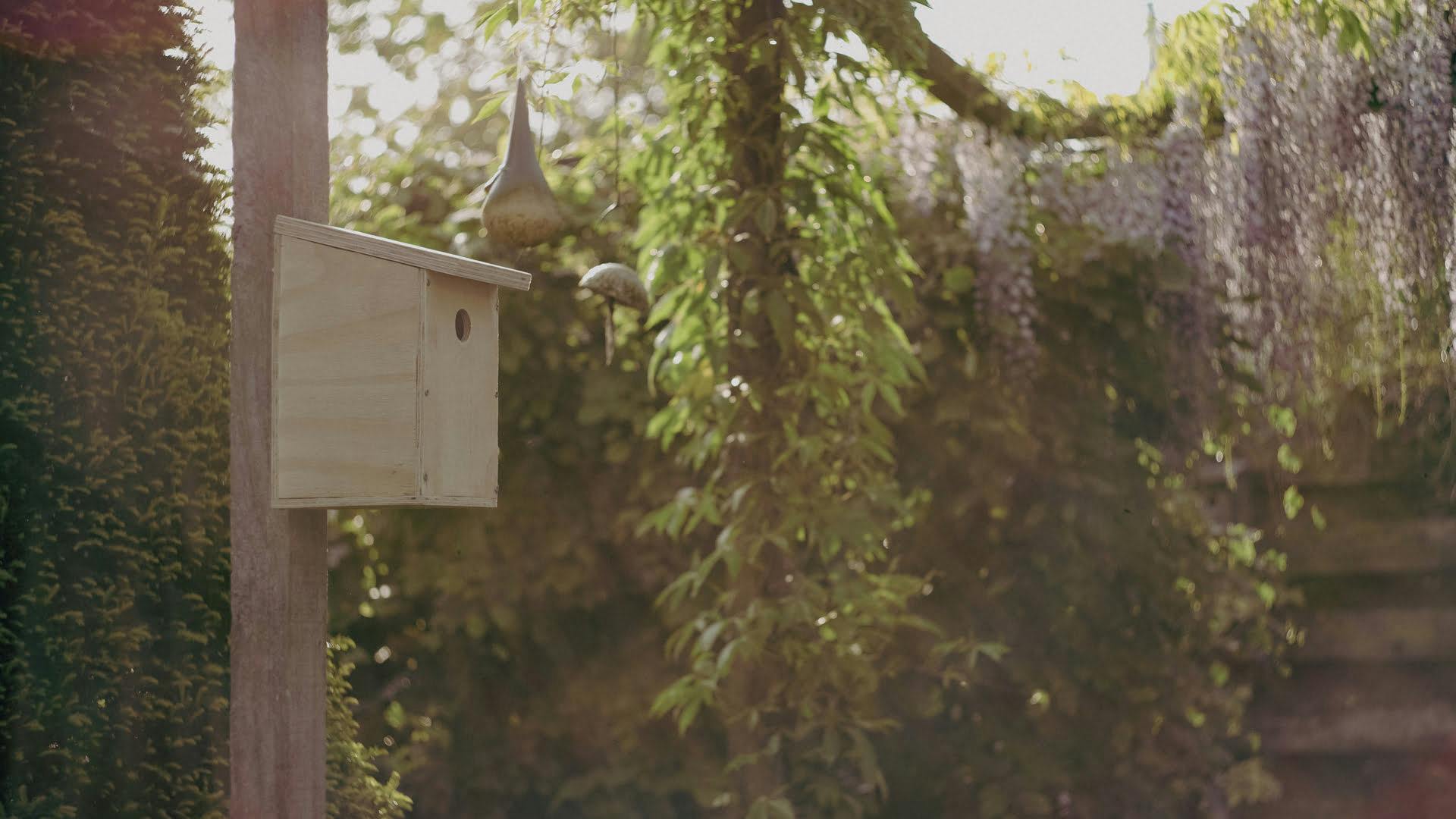 Het zelfgemaakte vogelhuisje hangt aan een paal in de tuin