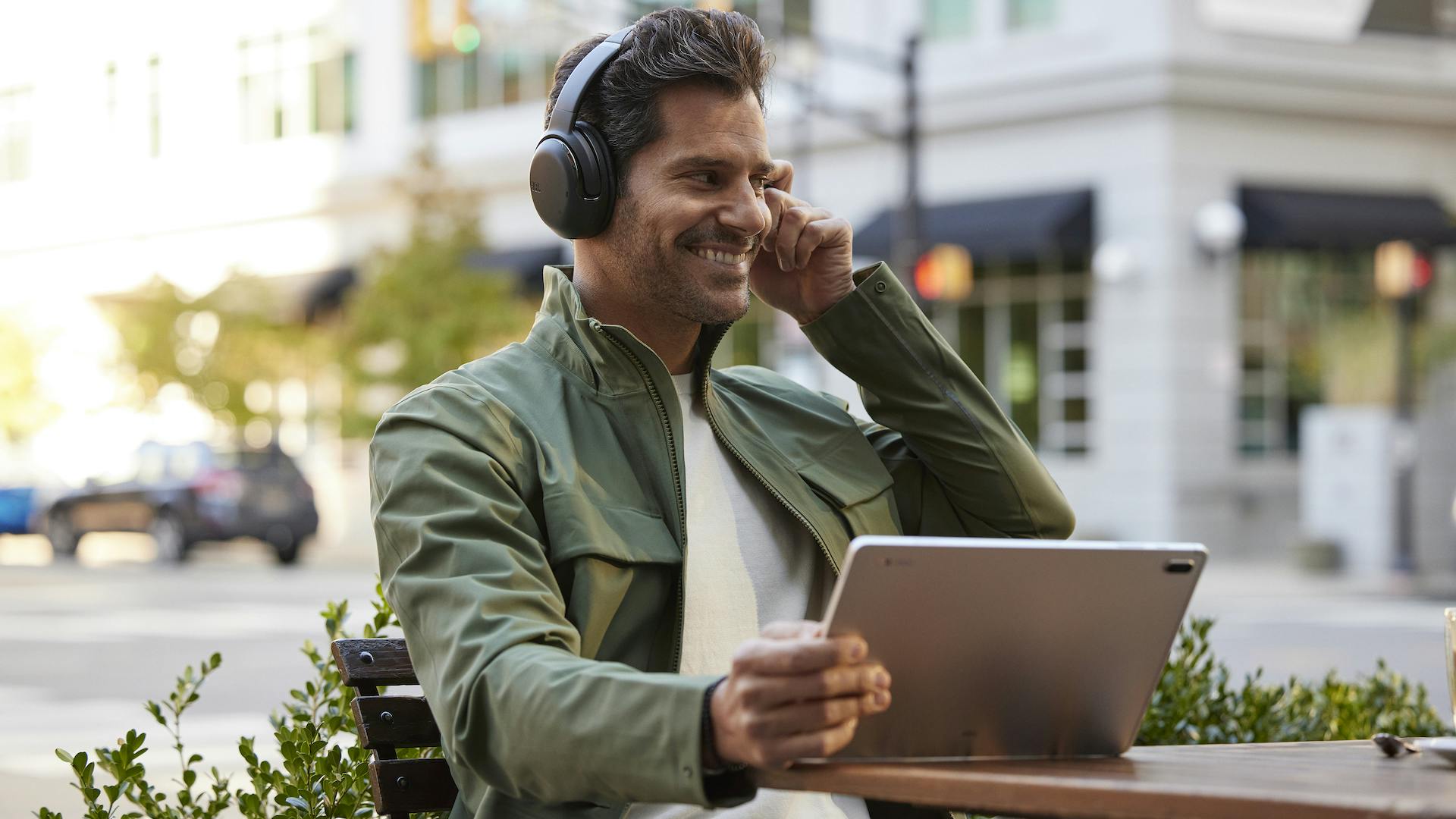 Man in stadsomgeving belt aan computer met JBL-hoofdtelefoon