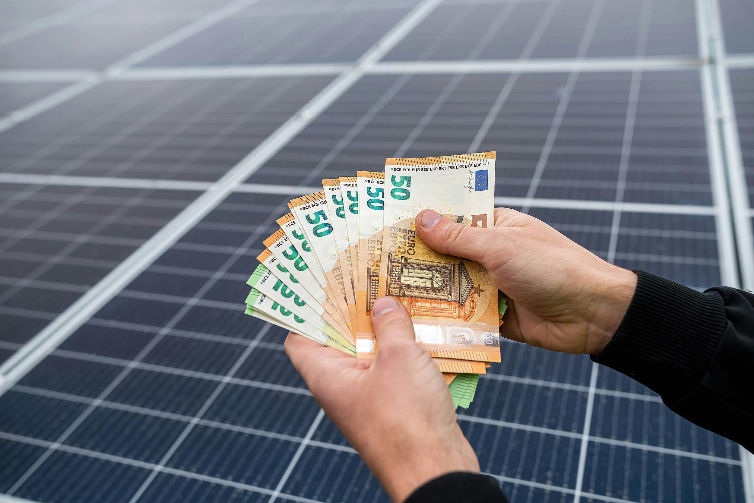 Iemand die eurobiljetten laat zien boven zonnepanelen