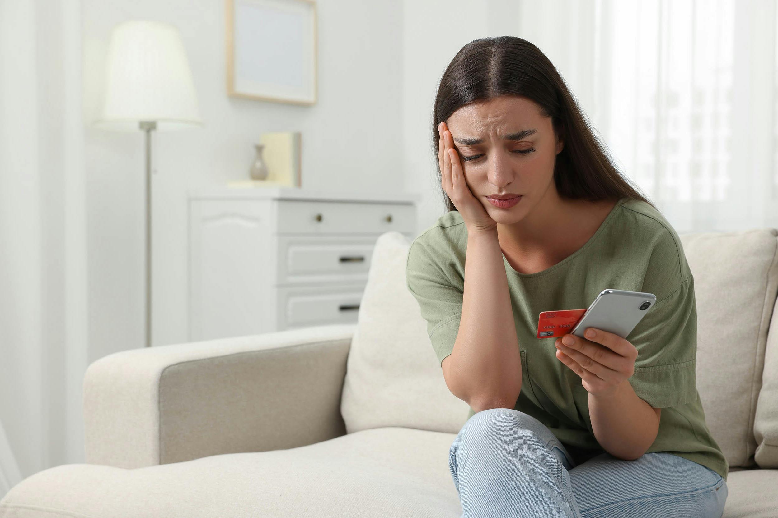 Vrouw die ongerust naar bankpas en smartphone kijkt