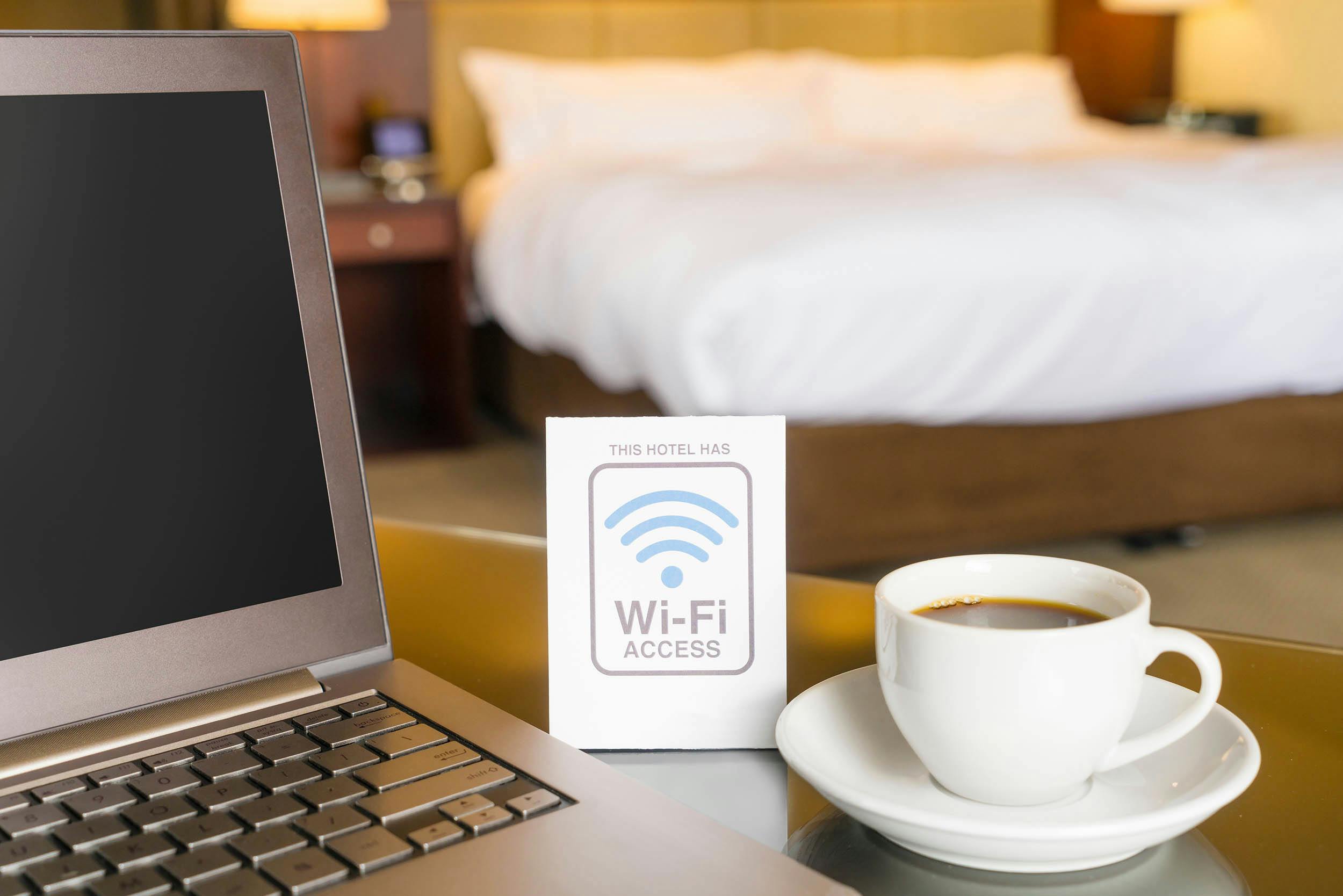kopje koffie met laptop in een hotelkamer en een free wifi bordje
