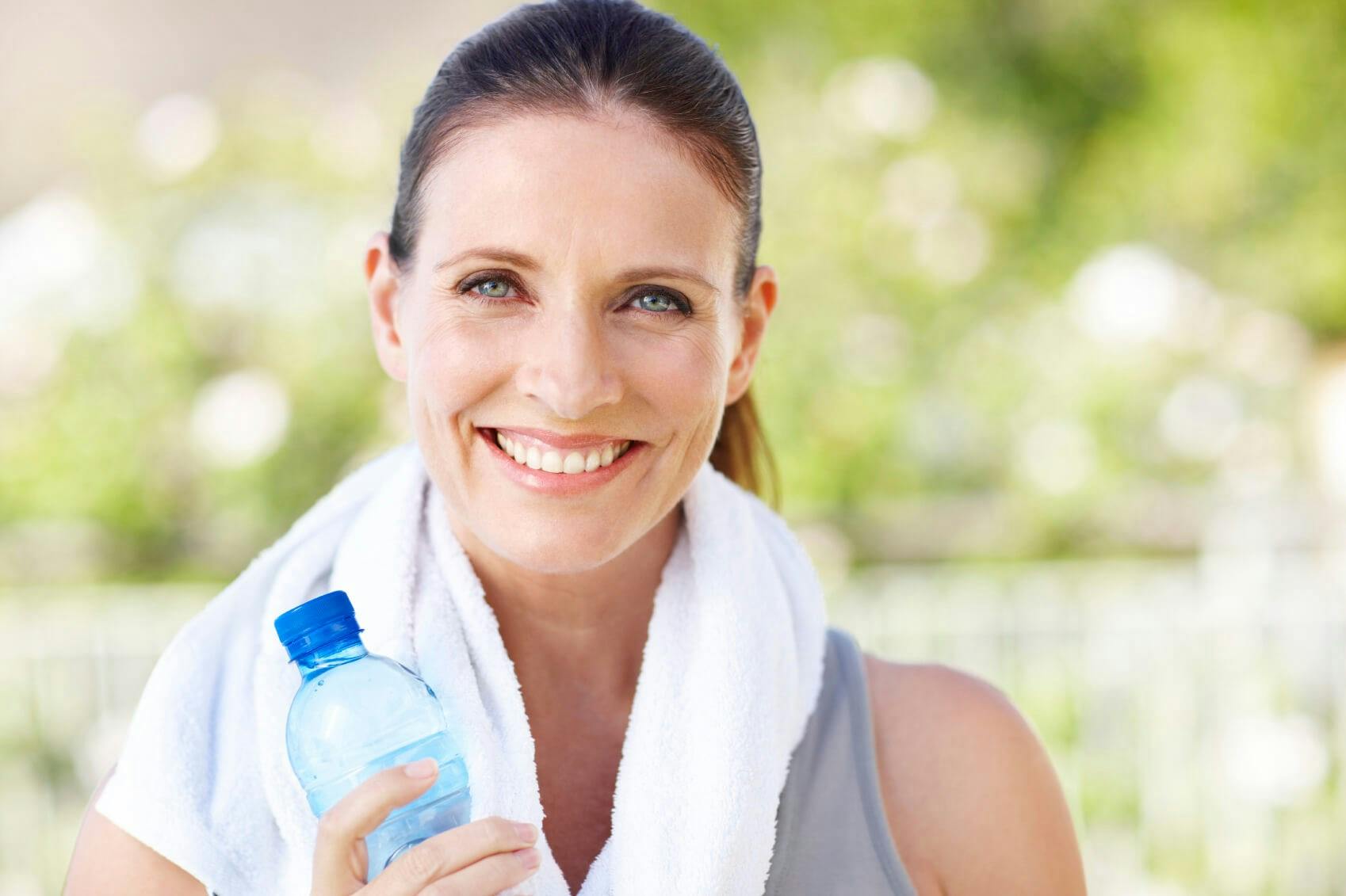 Woman with towel around her neck holding water bottle