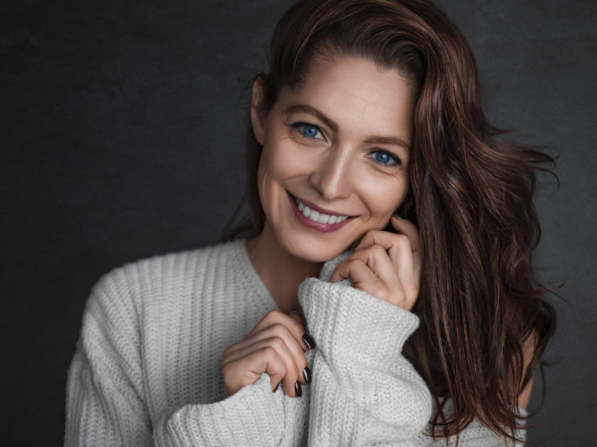 Woman smiling in grey sweater with hands to face