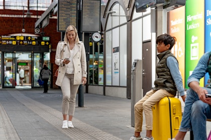 Kvinna på stationen går och tittar i sin mobiltelefon.