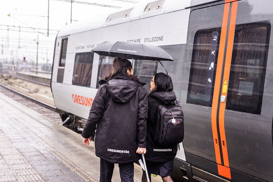 Två personer på perrong med paraply framför ett parkerat tåg