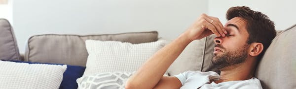 Man Laying On His Couch Holding His Nose