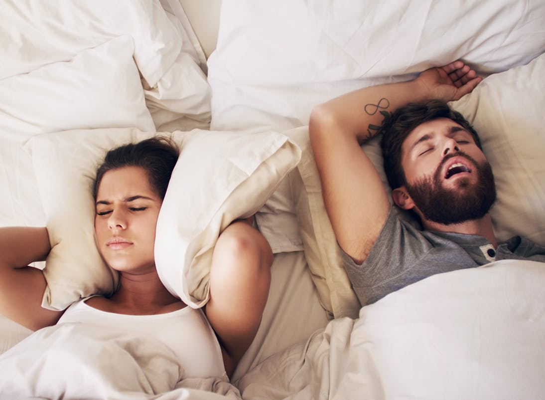 Woman annoyed by man snoring while they sleep in bed
