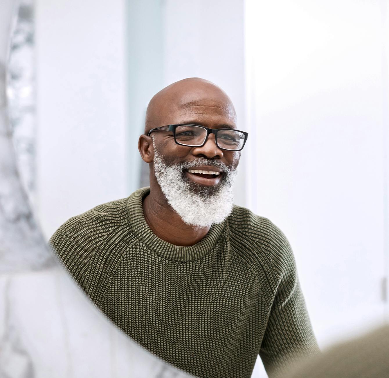 smiling man in green sweater and glasses looking at himself in mirror
