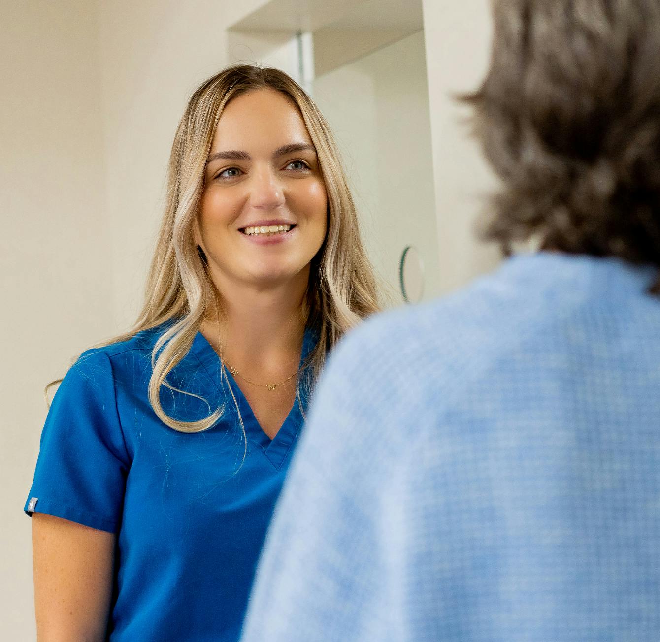 smiling woman in blue scrubs looking at herself in mirror