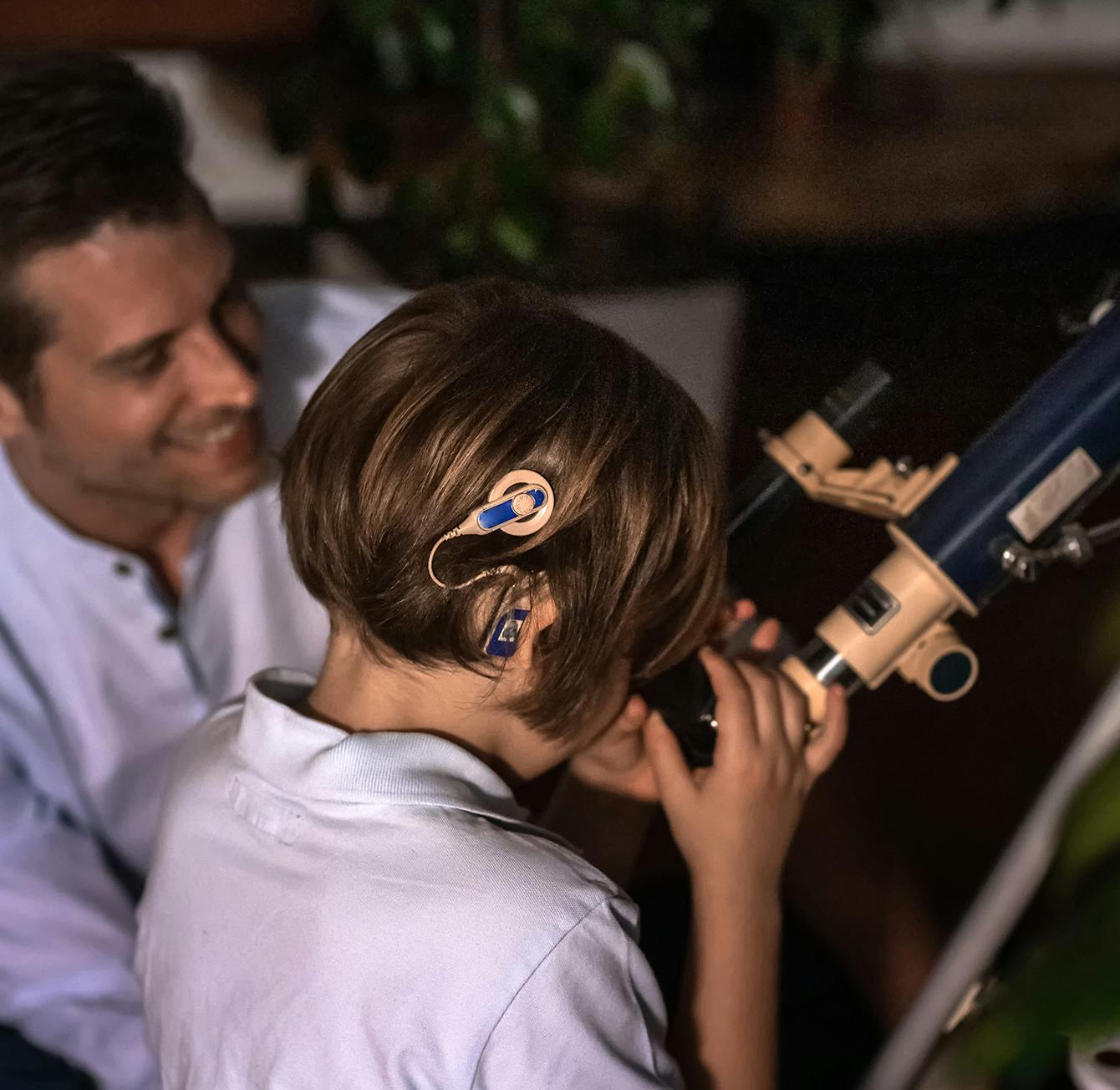 boy looking through a telescope with a man sitting beside him