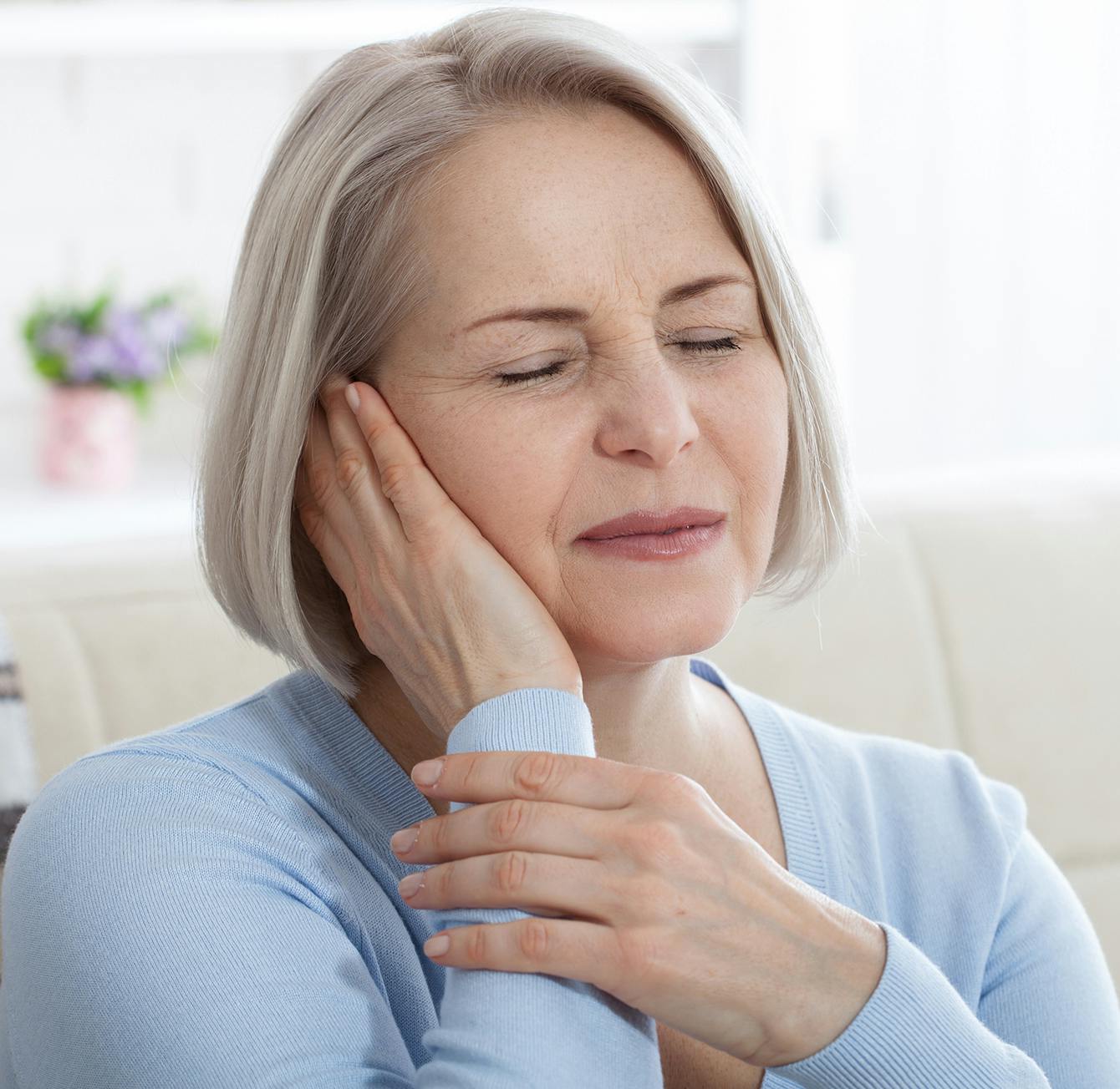 blond woman with closed eyes sitting on a couch with her hand on her face