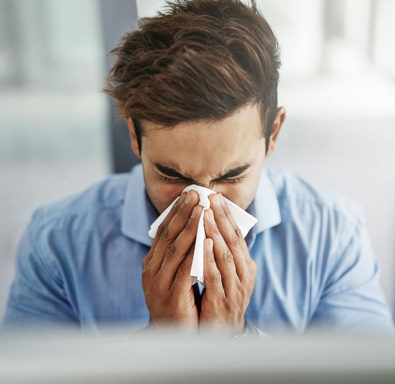 man blowing his nose with a tissue in front of his face