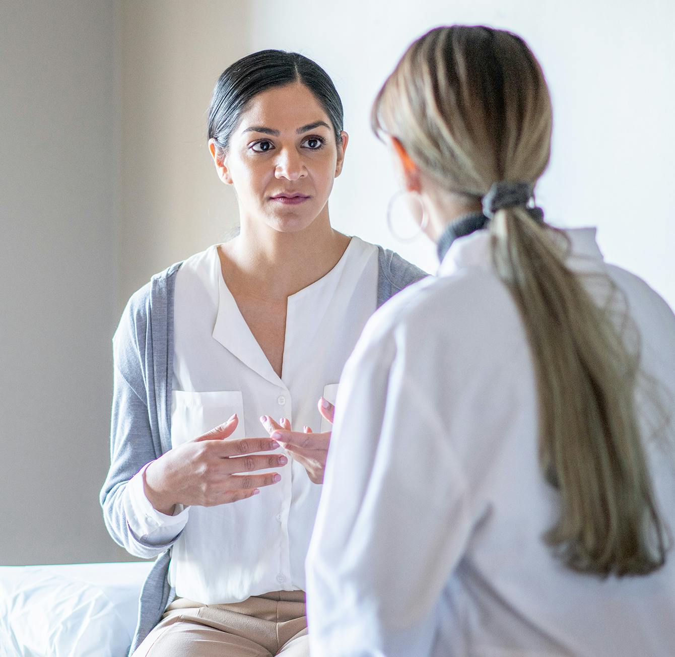 woman sitting on a bed talking to another woman in a white shirt