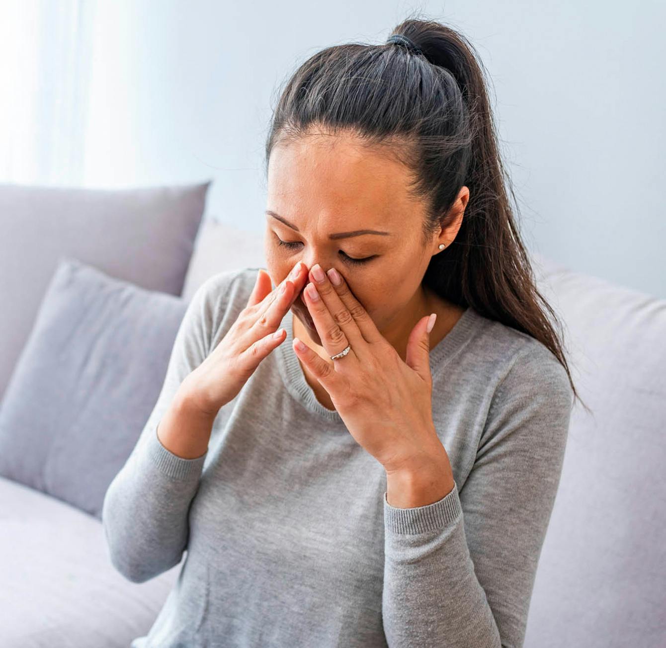 woman sitting on a couch rubbing her face with both hands