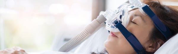 woman in a hospital bed with a mask on and a breathing device