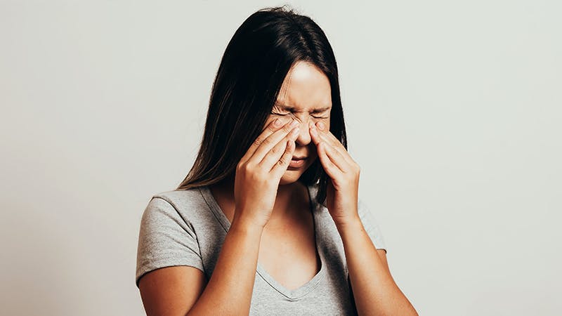 Woman with scrunched face and hands on her nose.