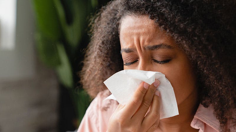 Black woman sneezing into a tissue