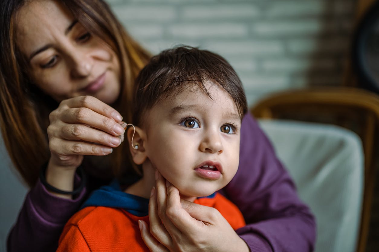 Mom helping child put on his hearing aid