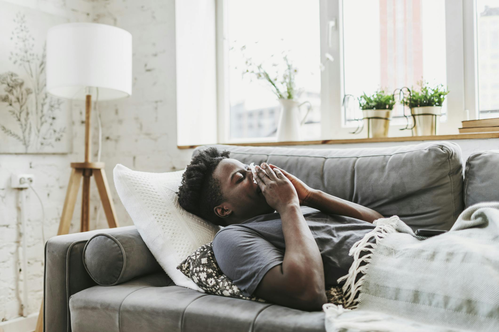 Sick man laying on the couch blowing his nose