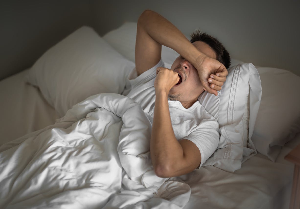 man lying in bed yawning