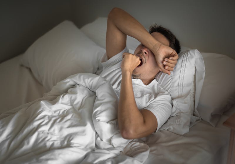 man lying in bed yawning