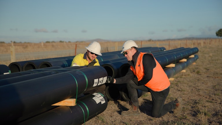 two men in hi-vis looking at large pipes