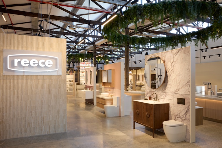 A look into the Reece showroom from the outside - On display is the Reece Logo, a brown vanity toilet, and greenery.
