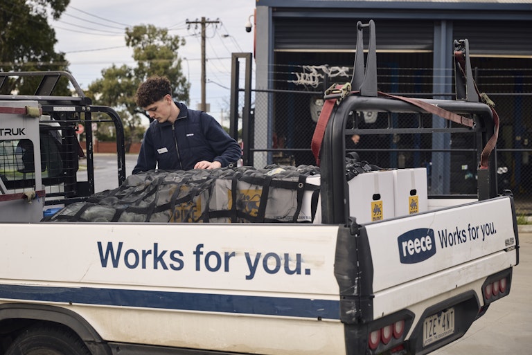 Reece woker placing pipe king box into back of Reece Ute - Side of ute reads "Works for you."