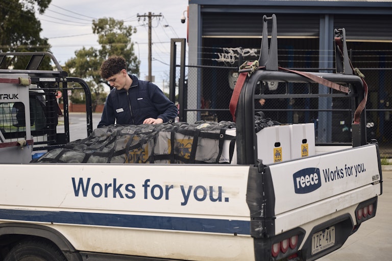 Reece woker placing pipe king box into back of Reece Ute - Side of ute reads "Works for you."