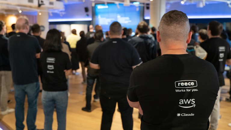 Man facing front of stage - Shirt reads Reece Works for you, with AWS (Amazon Web Services) & Claude logos.