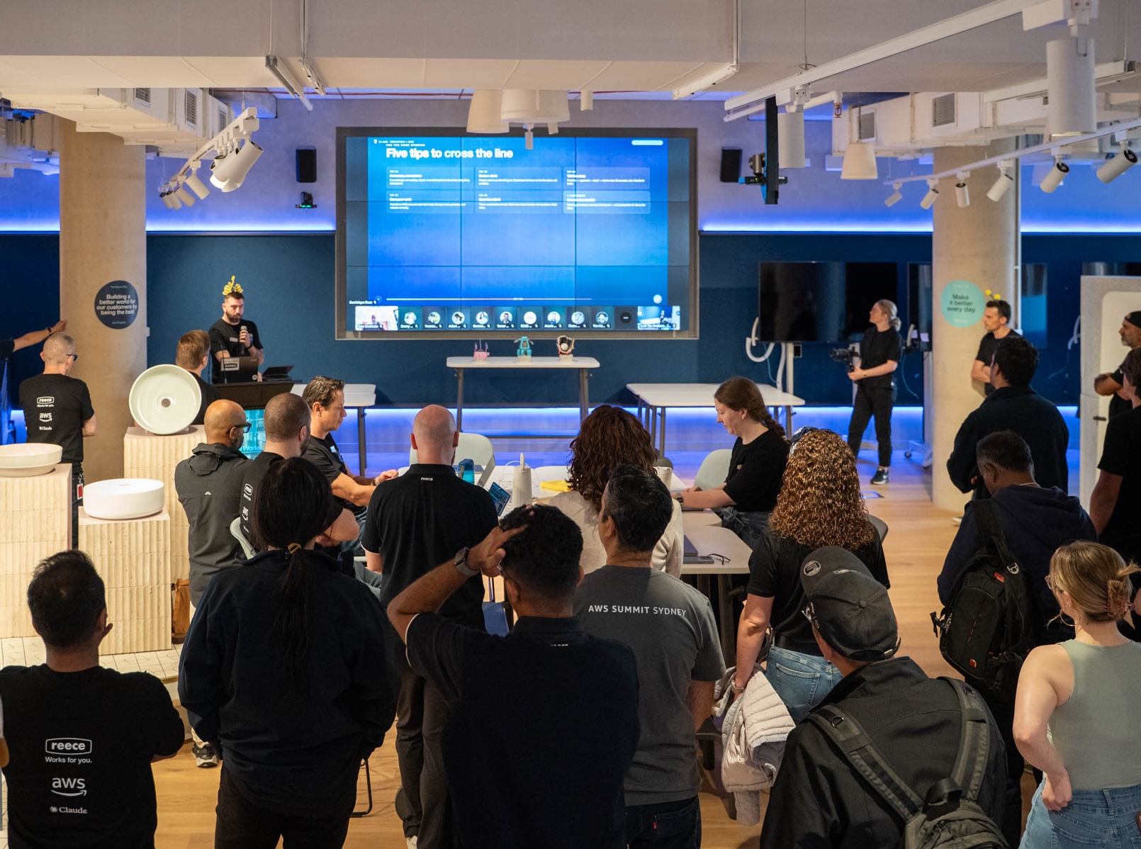 A crowd facing a screen, learning how they will present their solutions at the showcase