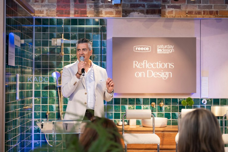 Michael standing with microphone talking to crowd - Sign in the background reads "Reece - Saturday indesign - Reflections on Design"