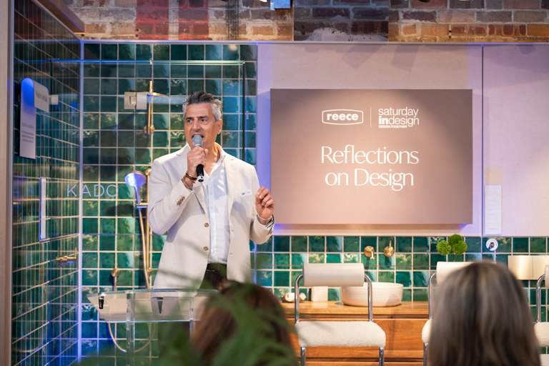 Michael standing with microphone talking to crowd - Sign in the background reads "Reece - Saturday indesign - Reflections on Design"