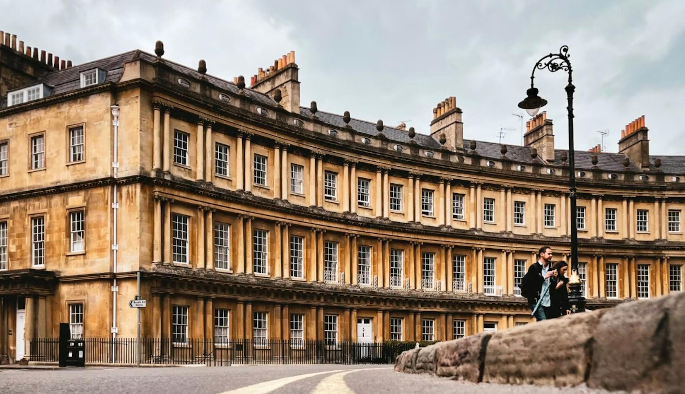 A curved Georgian terrace of golden stone townhouses with tall chimney stacks in Bath.