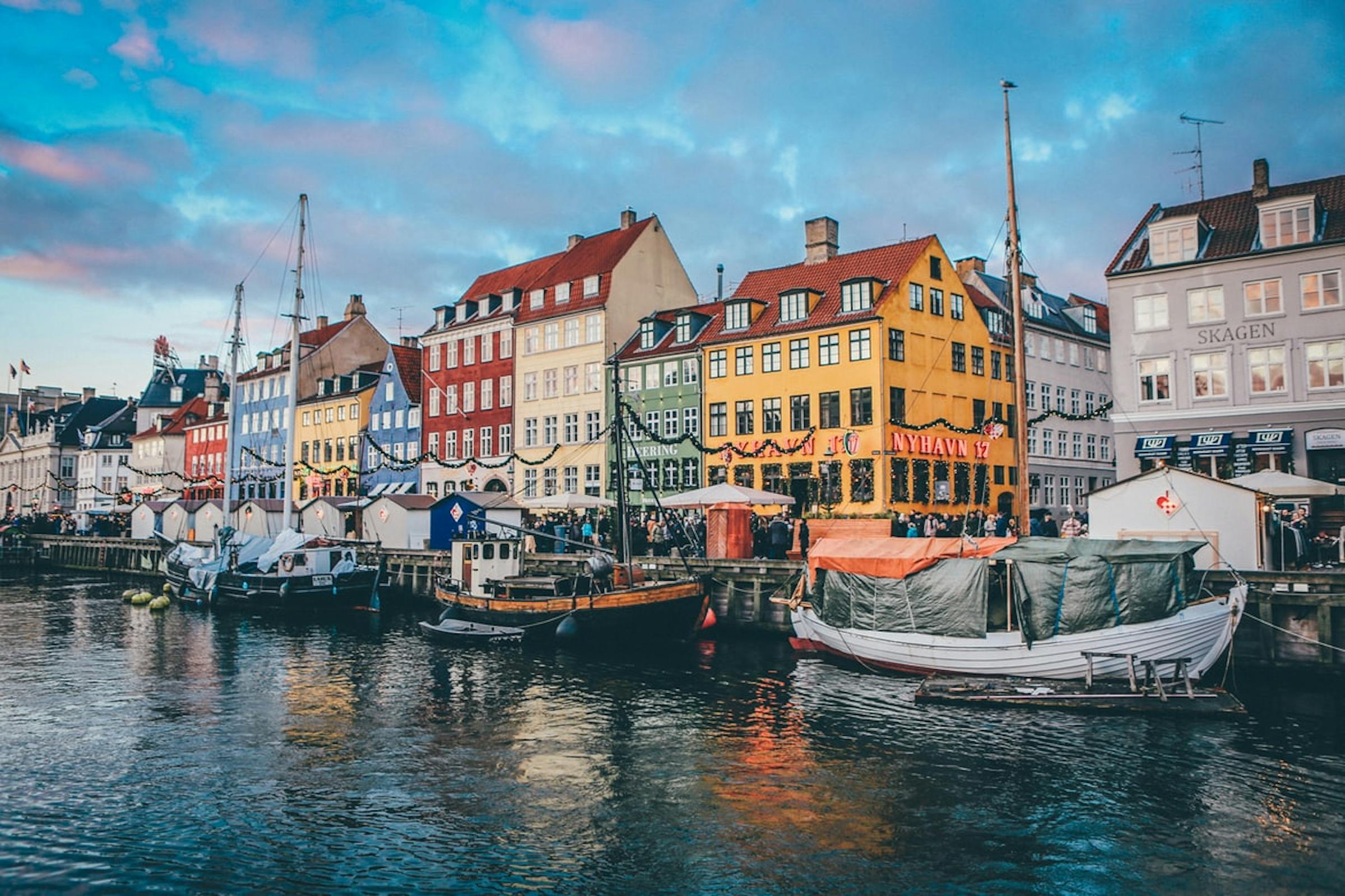 Colourful gabled houses and moored wooden boats line Copenhagen's Nyhavn canal at dusk.