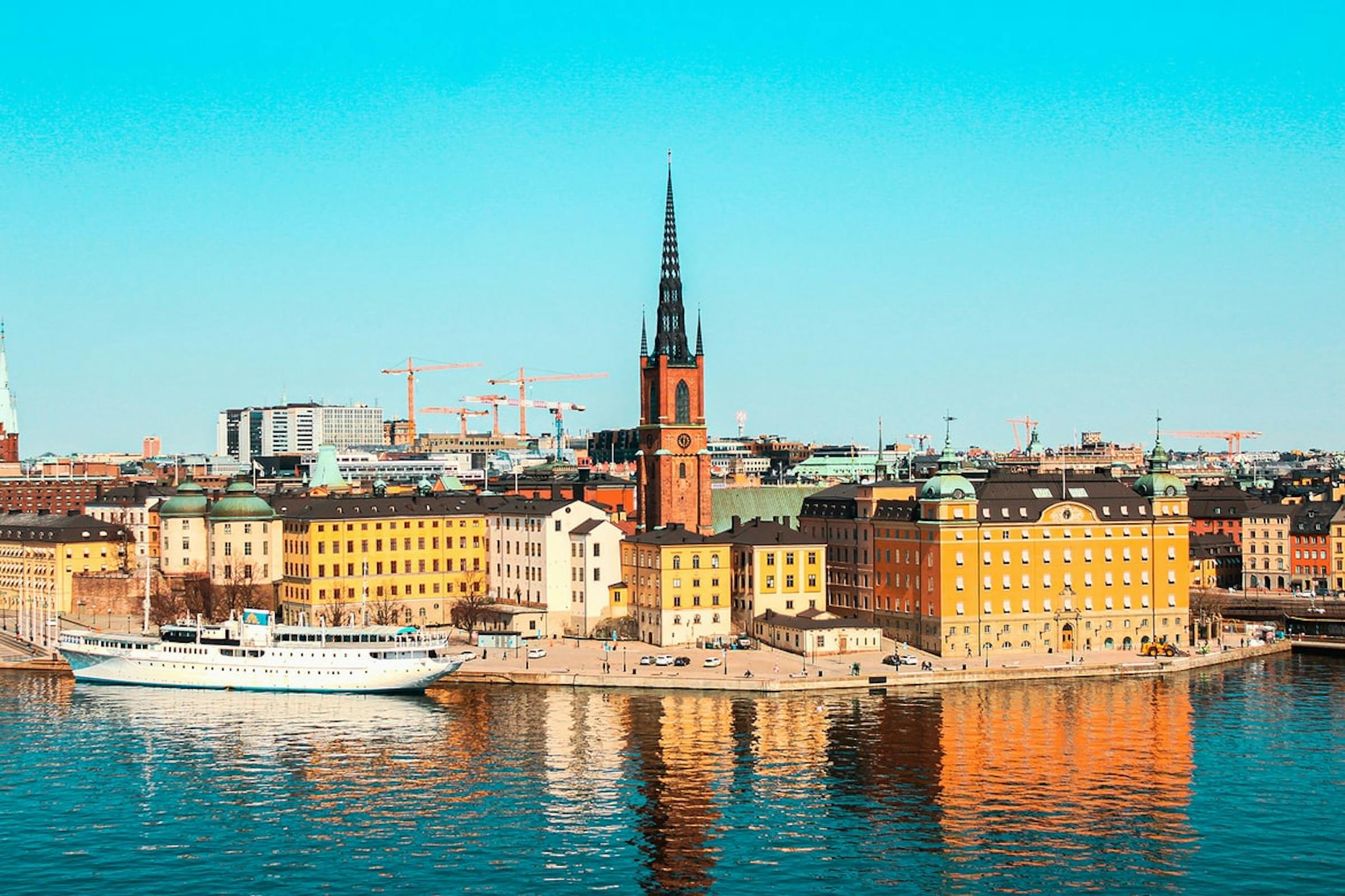 Riddarholmen Church's spire rises above Stockholm's old-town waterfront, with a boat moored at the quay.