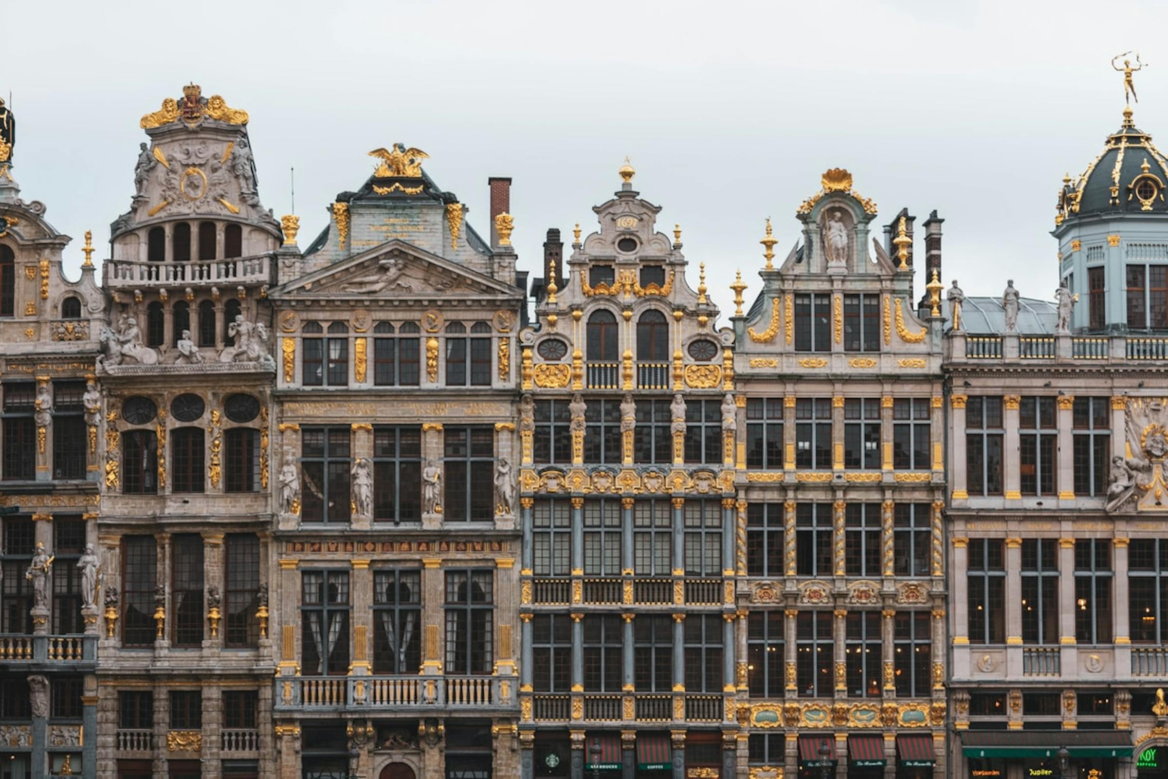Gilded baroque guildhall facades with statues and gold ornamentation line Brussels' Grand Place.
