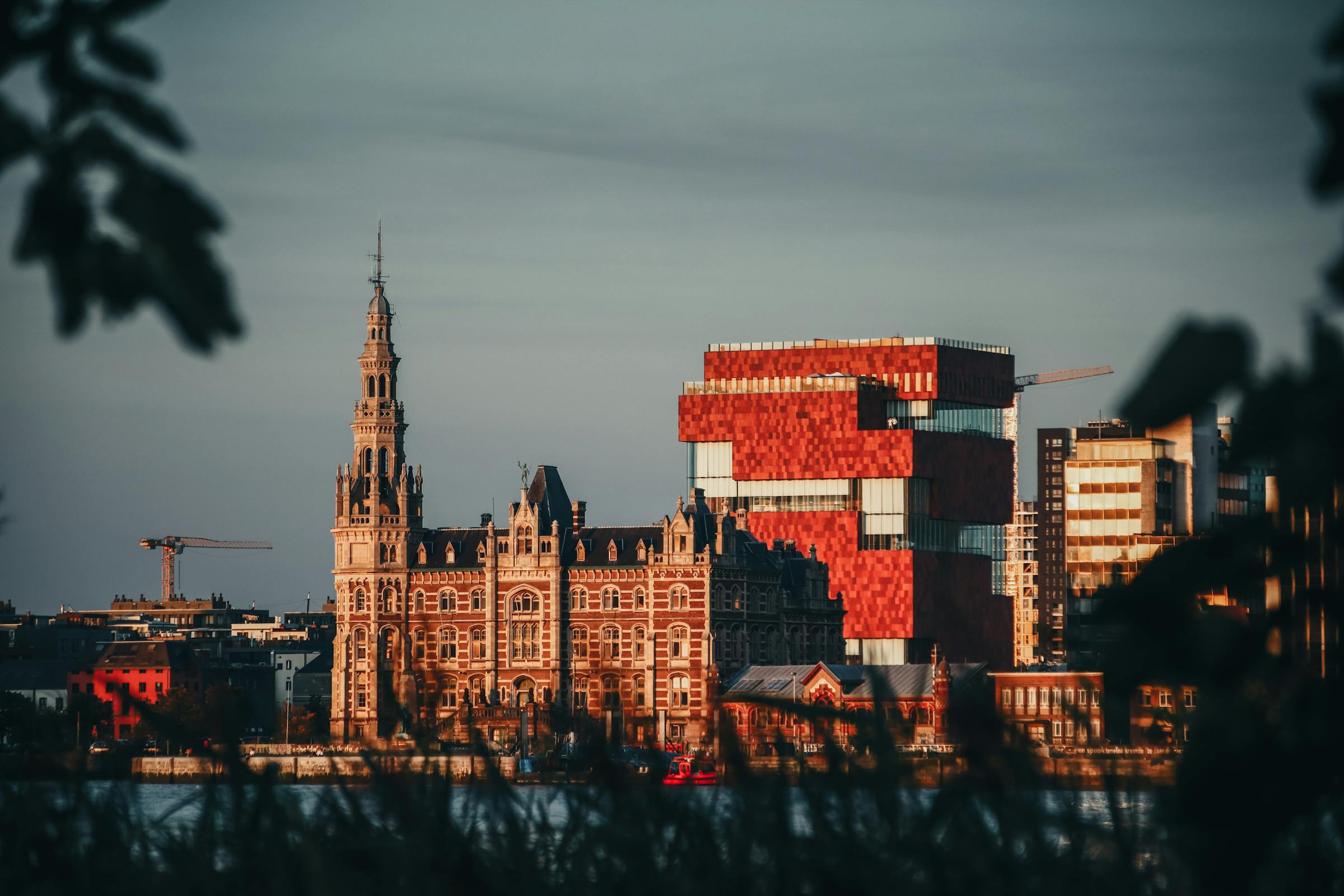 Antwerp's red-brick MAS museum rises beside a historic stone harbour tower at dusk.