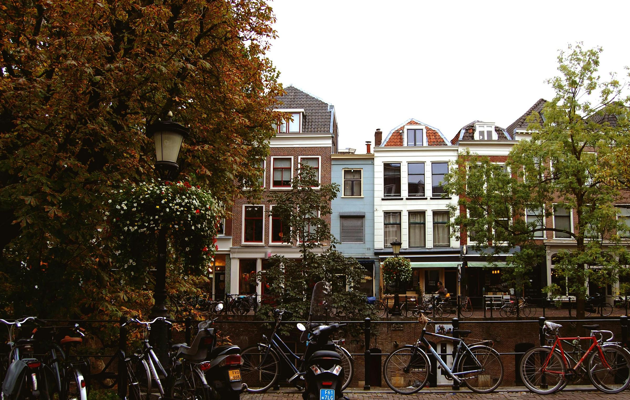 Bicycles line a canal railing in Utrecht, fronted by gabled townhouses and autumn trees.