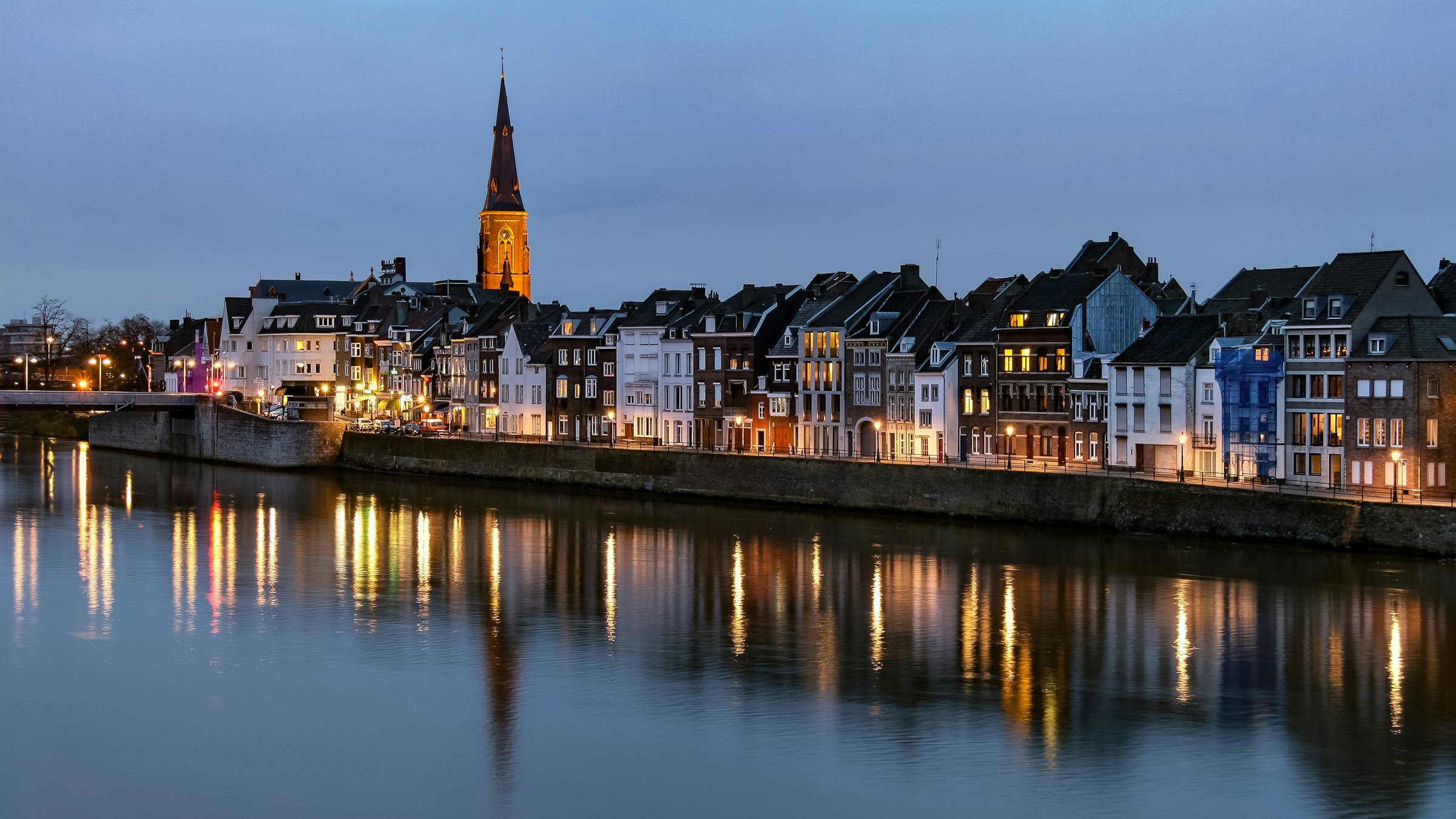 Maastricht's riverside skyline glows at dusk, a church spire and townhouses reflected in the Meuse.