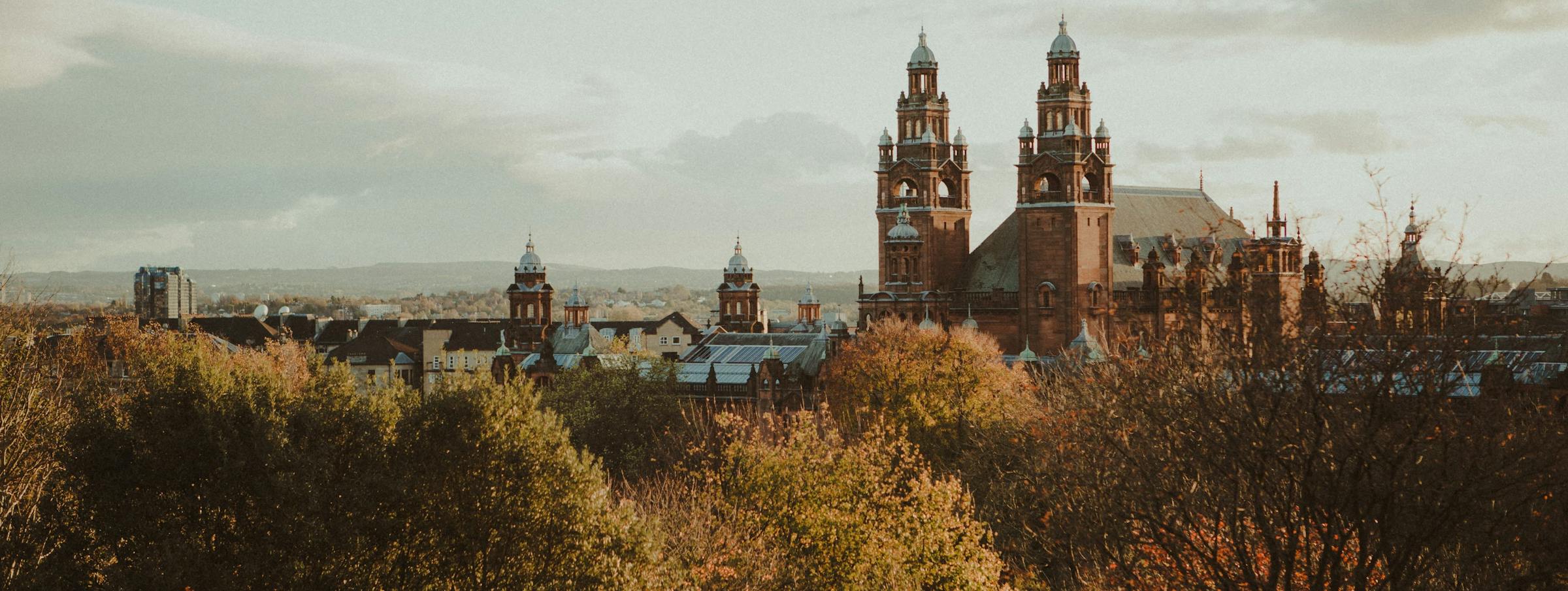 Kelvingrove Art Gallery's red sandstone towers rise above autumn trees in Glasgow.