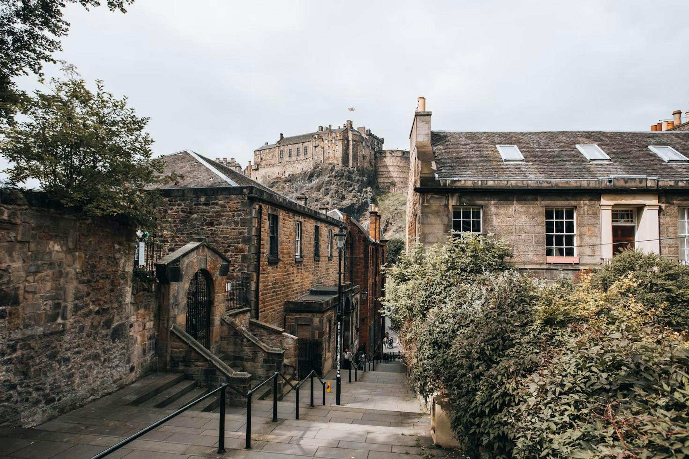 Edinburgh Castle looms above stone stairways and tenements in the Old Town on an overcast day.