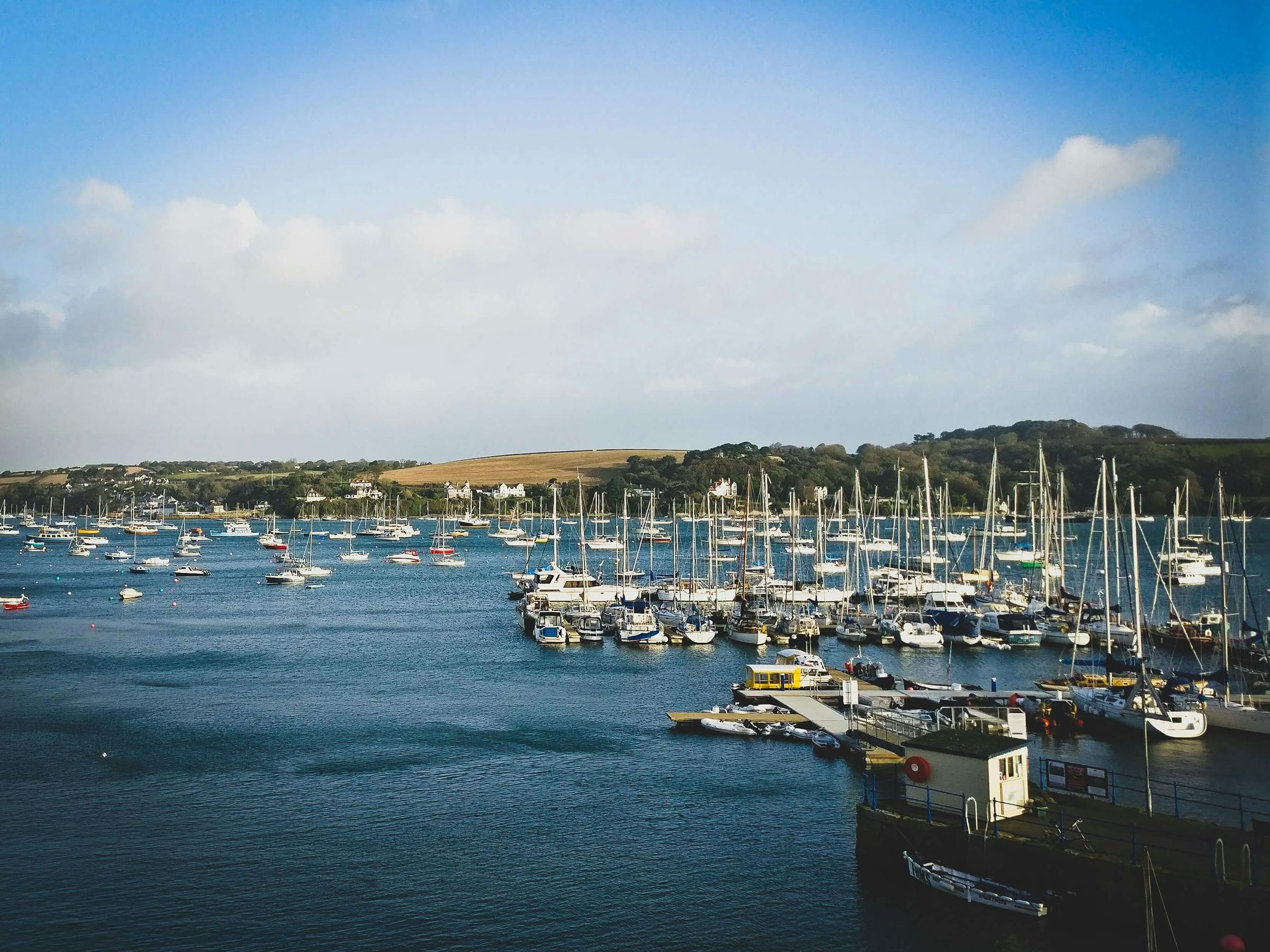 Rows of moored yachts fill Falmouth harbour, with green Cornish hills in the background.