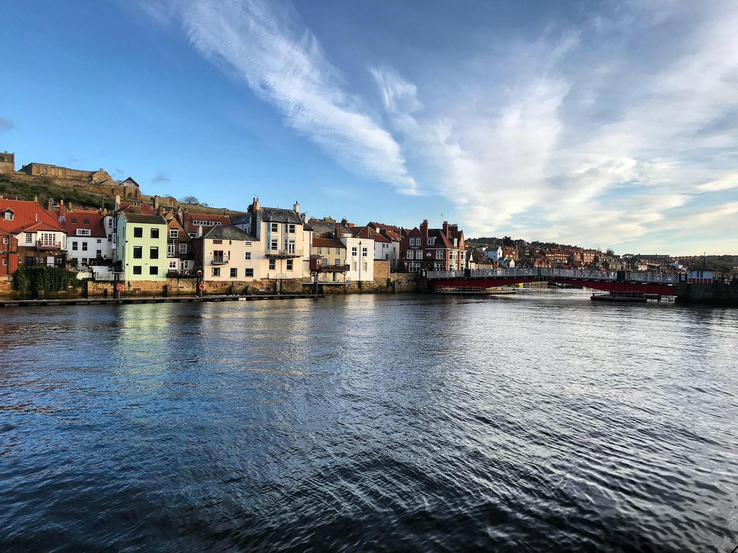 Whitby's harbourfront houses and a swing bridge sit below the hilltop ruins of Whitby Abbey.